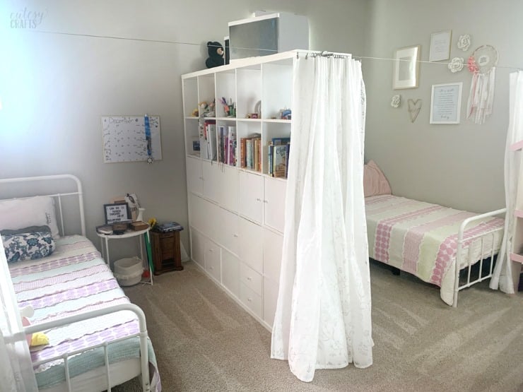 White IKEA KALLAX bookshelf used as a room divider between two twin beds.