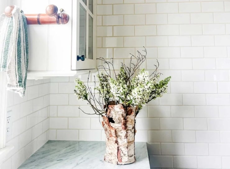 Birch bark vase with flowering branches on a marble countertop in a white subway tile kitchen