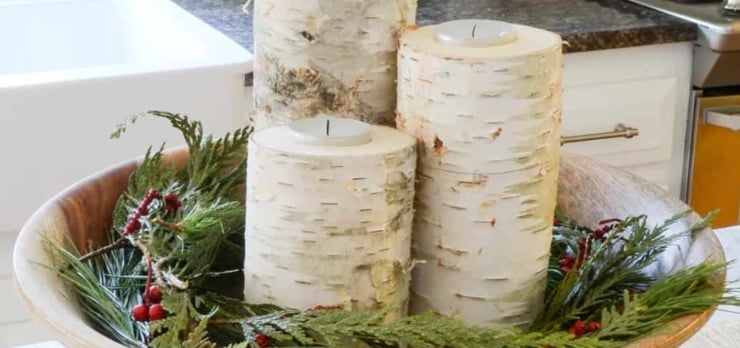 DIY birch candle holders displayed in a wooden bowl with evergreen sprigs and red berries
