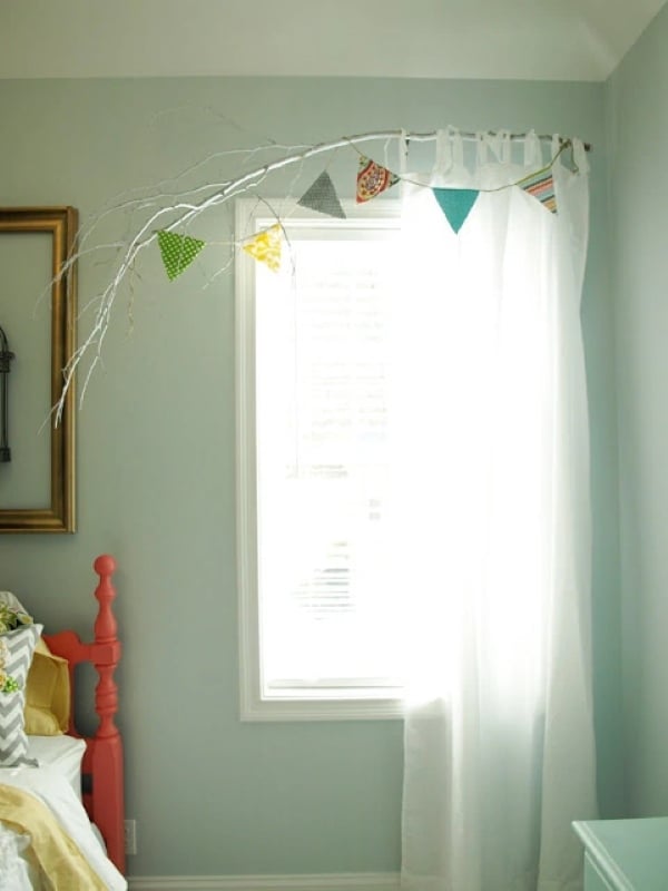 White painted tree branch used as a unique curtain rod with colorful fabric bunting in a bedroom