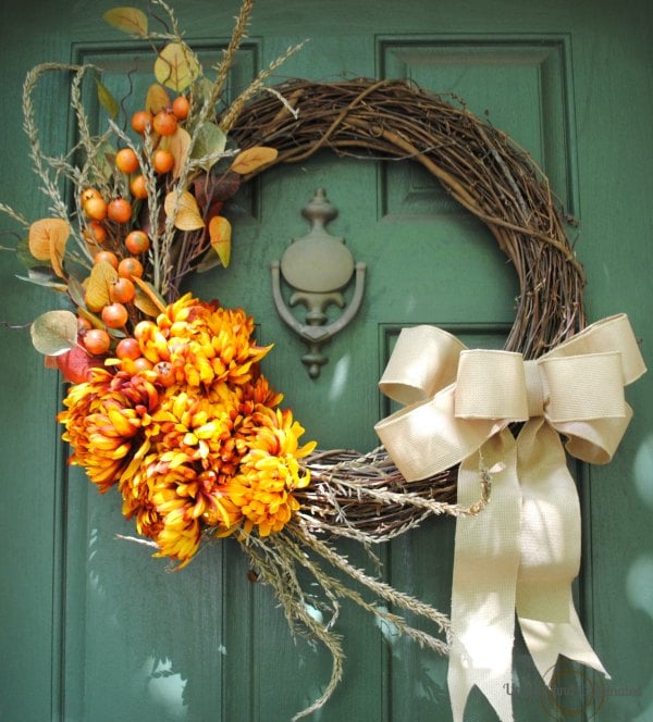 Grapevine fall wreath with orange flowers, berries, and a large cream bow
