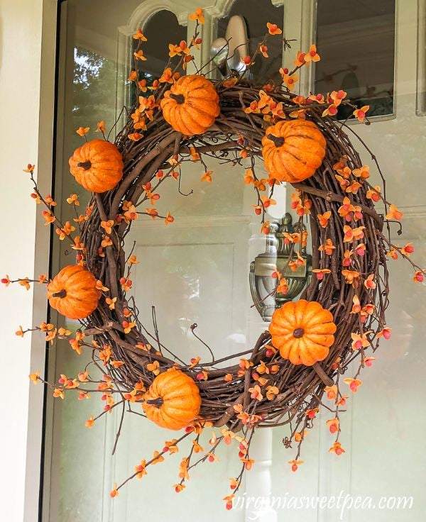 Grapevine fall wreath decorated with orange pumpkins and bittersweet branches