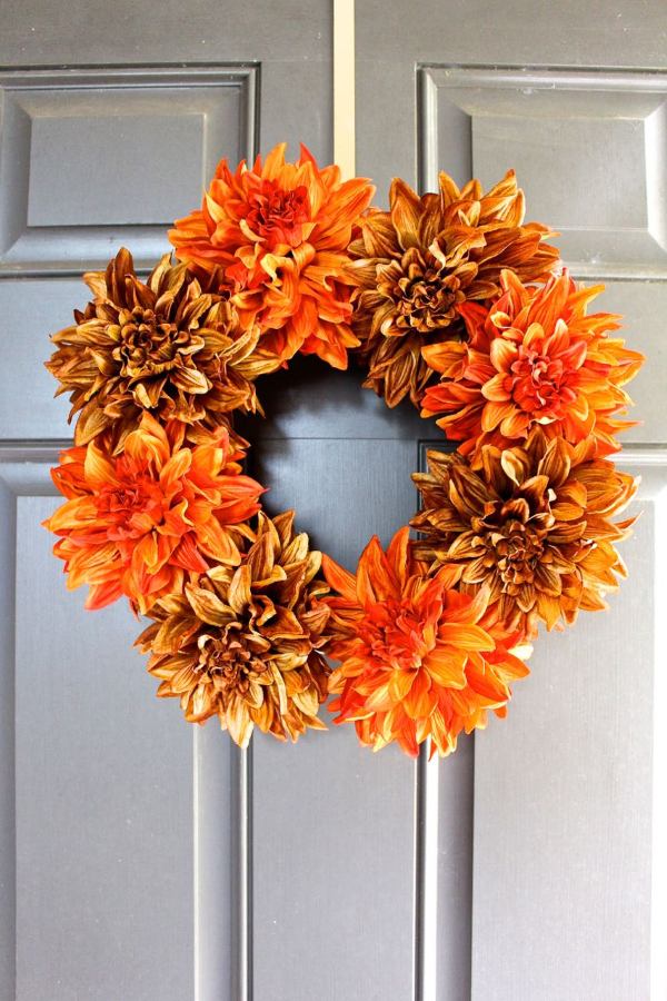 Orange and brown floral fall wreath hanging on a gray front door