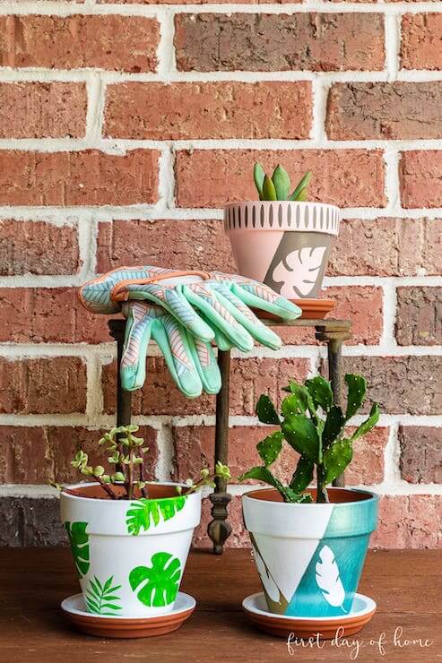 three terra cotta pots painted white and green and blue with leave shapes