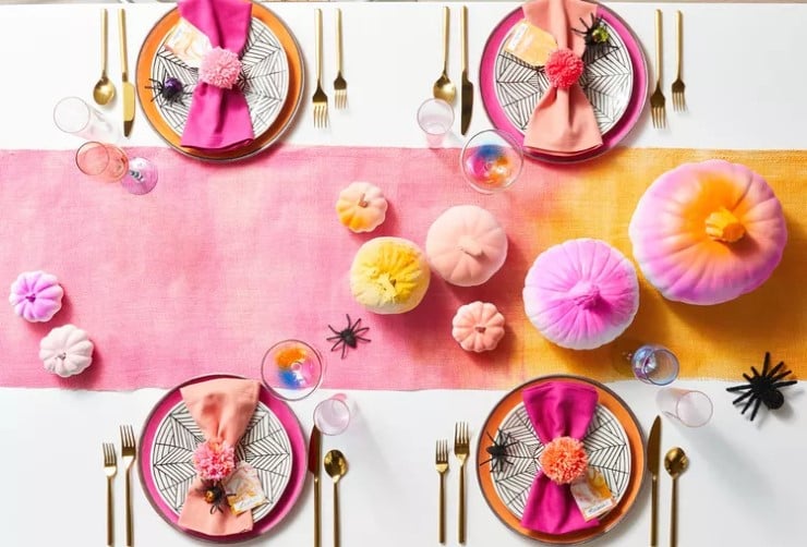 Bright pink and orange Halloween table setup with pumpkins, spiders, and gold utensils