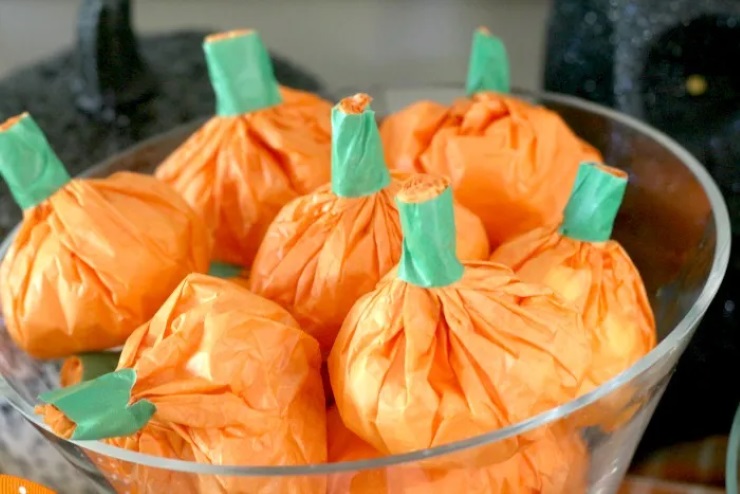 DIY orange tissue paper pumpkin party favors with green paper stems in a bowl