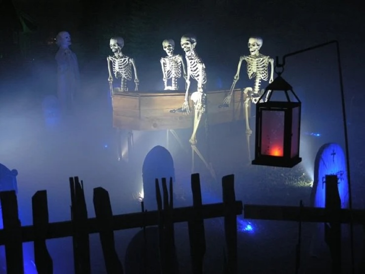 Outdoor haunted house scene with skeletons, gravestones, fog, and eerie lantern lighting
