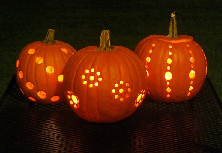 Three carved pumpkins glowing with creative polka dot patterns on a dark table