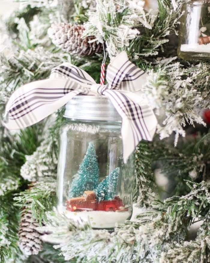 diy snow globe ornament with trees and a mini car figurine inside hanging from a tree