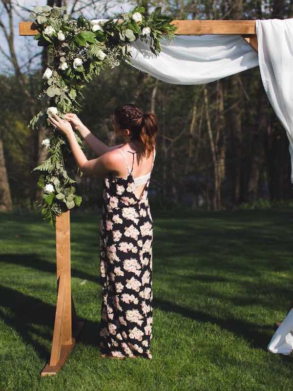 woman adding florals to a DIY wooden wedding arch or arbor