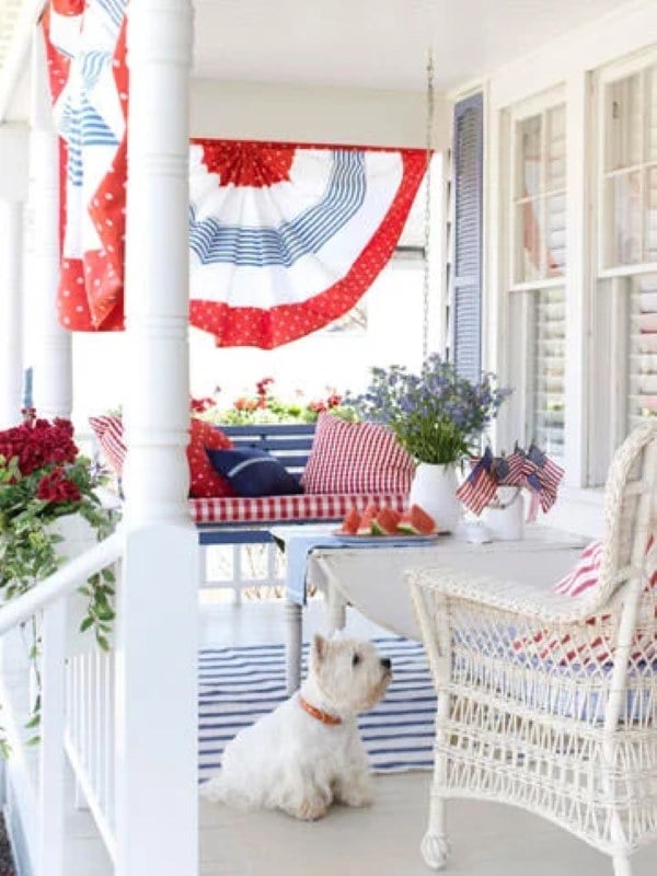 Front porch decorated with red white and blue pillows, flags, banners, and flowers