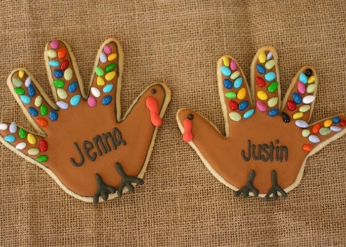 cookies cut in the shape of a handprint and decorated to look like turkeys
