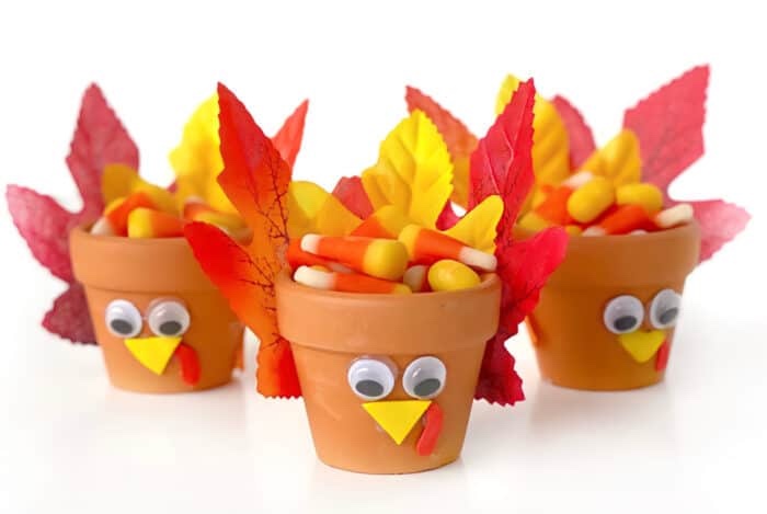 miniature plant pots made to look like turkeys with simple craft supplies and fake leaves filled with candy corn