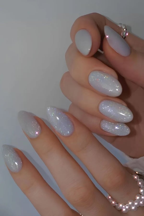 Almond-shaped nails in frosty white with subtle iridescent glitter for a snowy holiday look.