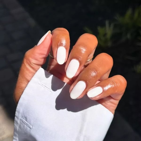 Hand with smooth, glossy white nails shown in sunlight for a bright winter look.