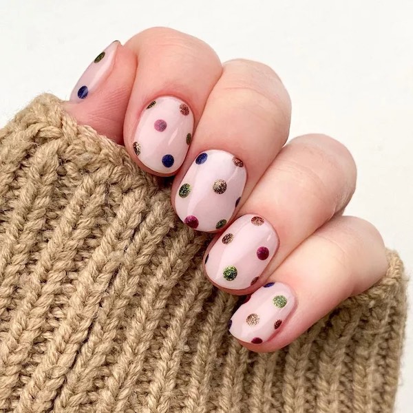 short nude pink nails with evenly spaced polka dots of glittery holiday colored polish