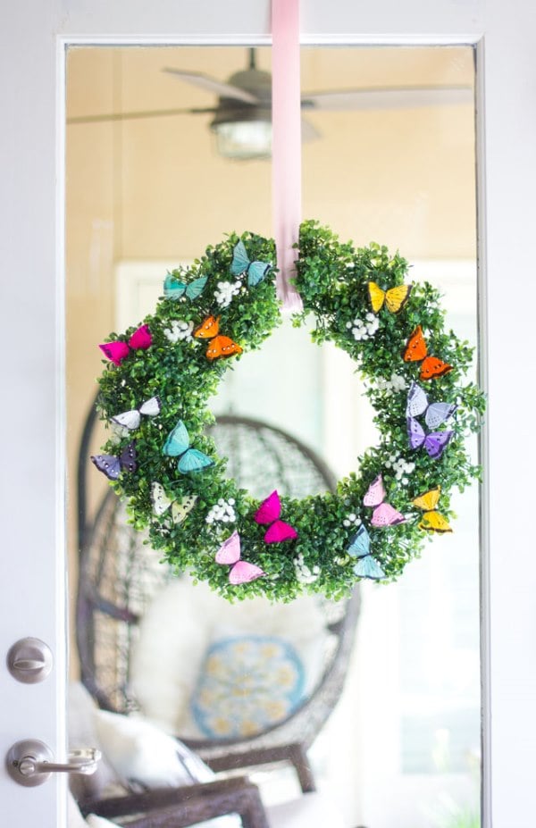 Green boxwood spring wreath decorated with colorful butterfly accents hanging on a glass door