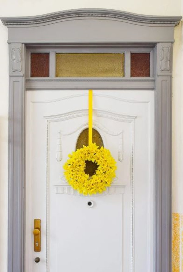 Bright yellow daffodil spring wreath hanging on a white front door with ribbon
