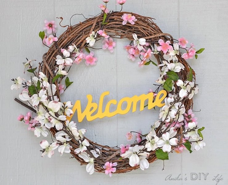 Simple grapevine spring wreath with pink and white faux flowers and a welcome sign