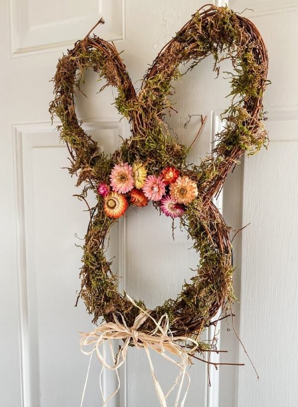 Bunny shaped moss spring wreath with dried flowers hanging on a white door