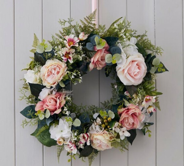 Pink faux flower spring wreath with layered petals and gingham ribbon on a light surface