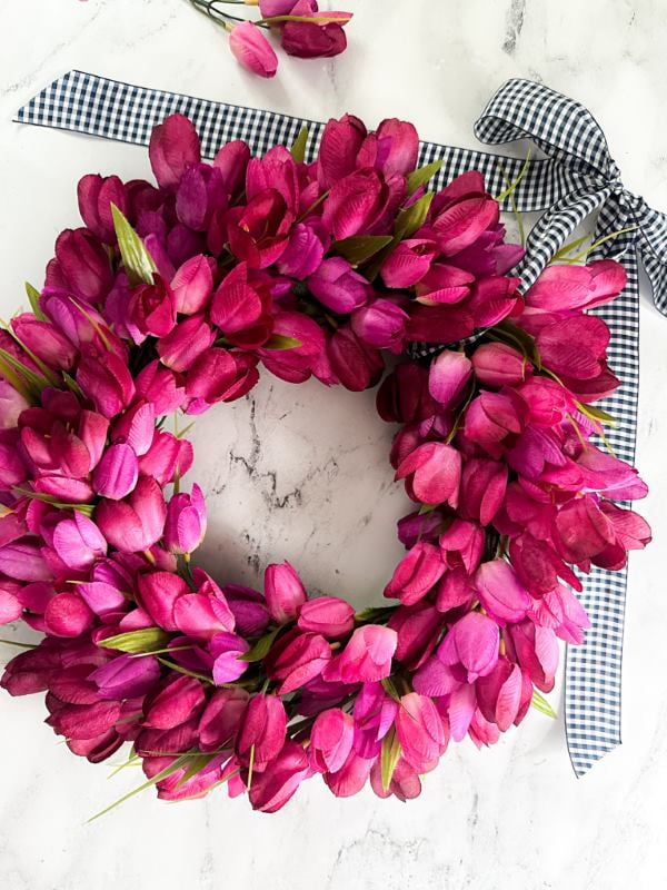 Soft pink and cream floral spring wreath with tulips and greenery hanging on a light wood door