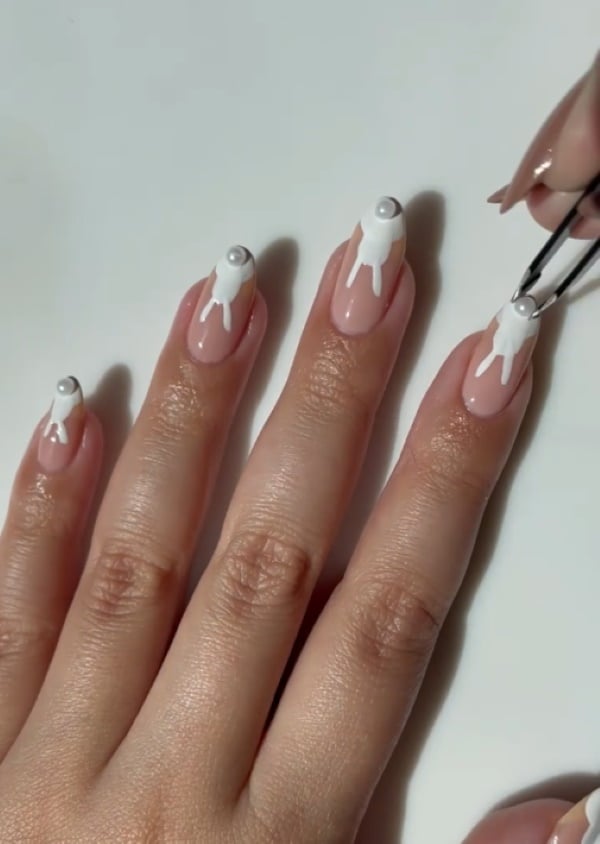 Neutral pink nails with white bunny designs and pearl accents for a simple Easter manicure.