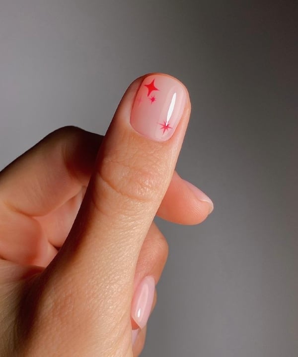 Minimalist nude nails with tiny red firework stars for simple summer nail art