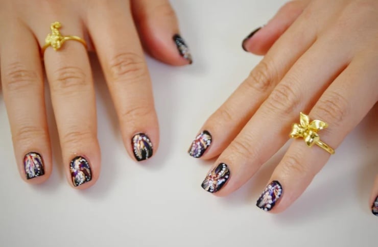 Black firework nails with glittery patriotic sparkler designs and gold rings styled on hands