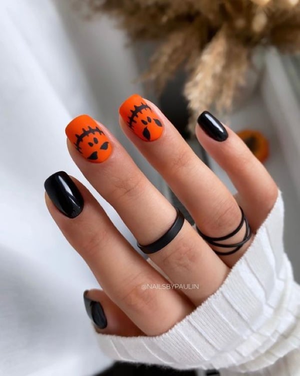 Black and bright orange nails with two orange accent nails featuring black jack-o'-lantern faces.