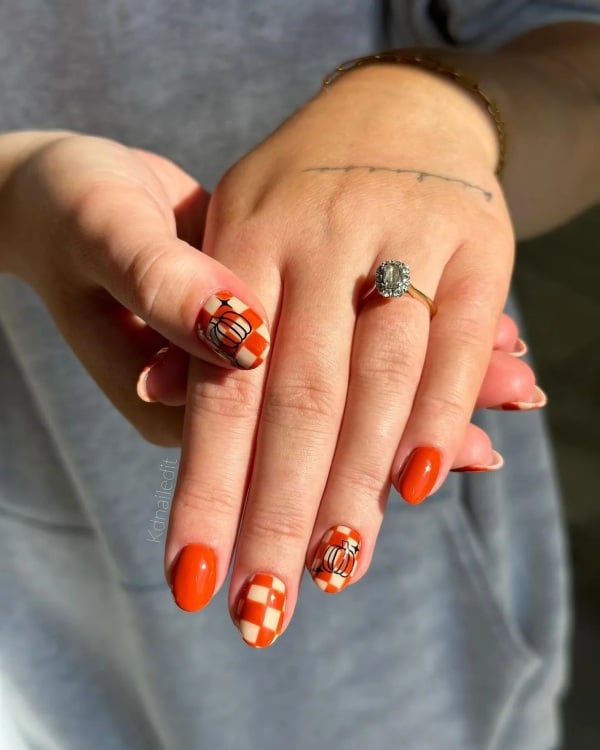 Bright orange nails with orange-and-white checkered accent nails featuring outlined pumpkins.