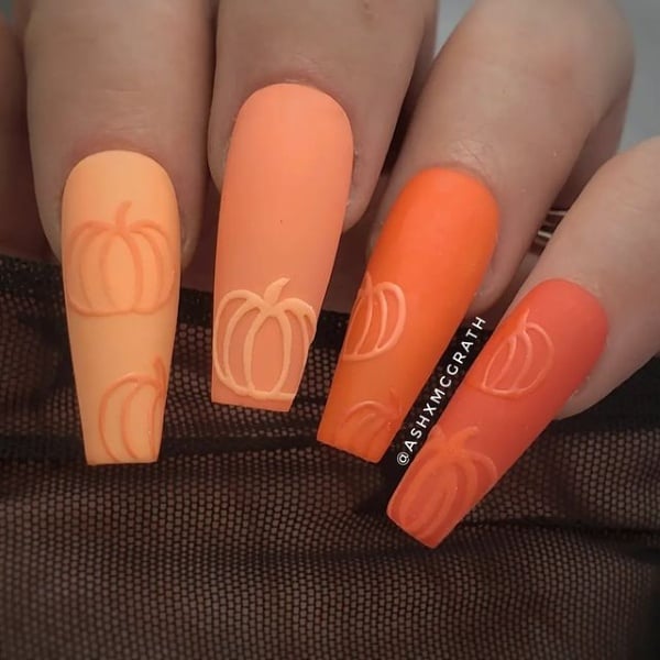 Long square nails in varying shades of peach and orange with subtle outlined pumpkin designs.