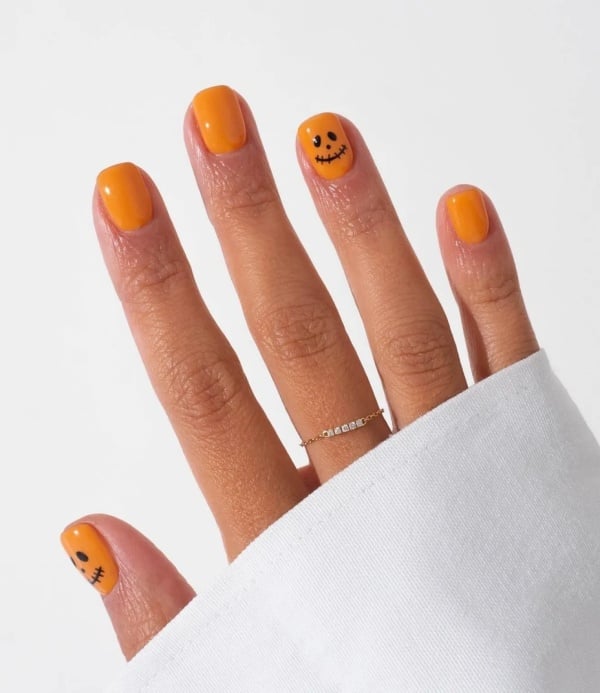 Short bright orange nails with small black jack-o'-lantern faces painted on two accent nails.