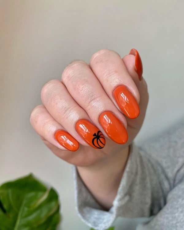 Glossy orange nails with a simple black outlined pumpkin on one accent nail.