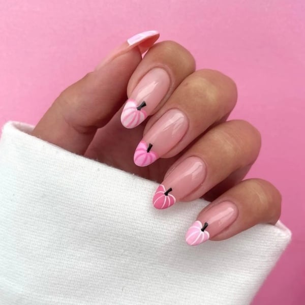 Pale pink almond-shaped nails with pink pumpkin designs incorporated into the French tips.