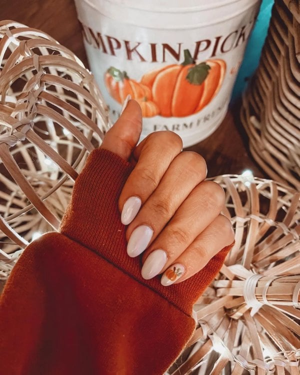 Glossy white almond-shaped nails with a small orange pumpkin painted on one accent nail.