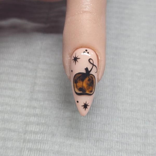 Nude almond-shaped nail with a brown tortoiseshell pumpkin surrounded by small black stars, dots, and line details.